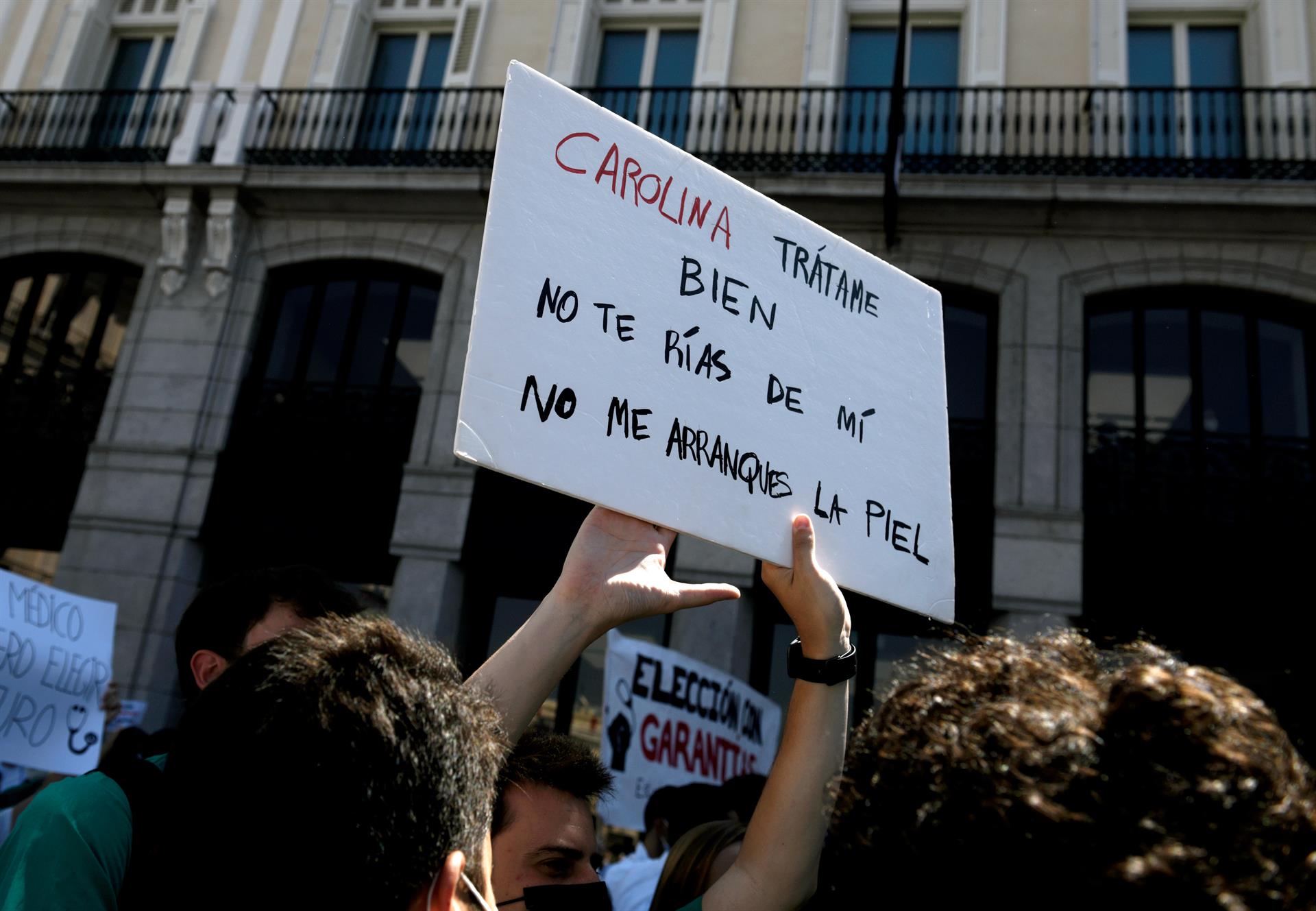 Persona sujetando y levantando una pancarta frente a la Puerta del Sol para exigir una elección de plazas con garantías