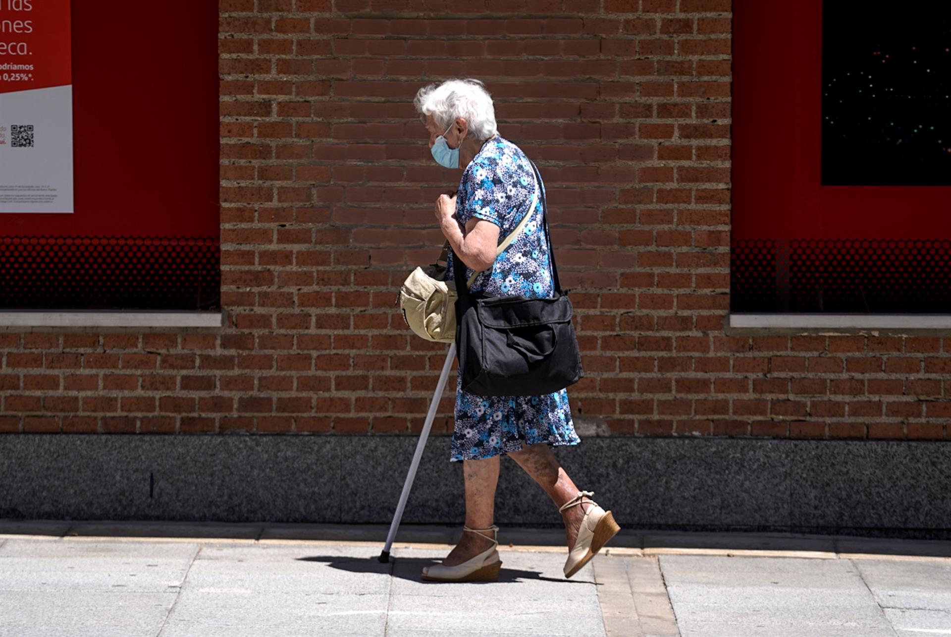 Una anciana con mascarilla camina por la calle ayudada de una mulet