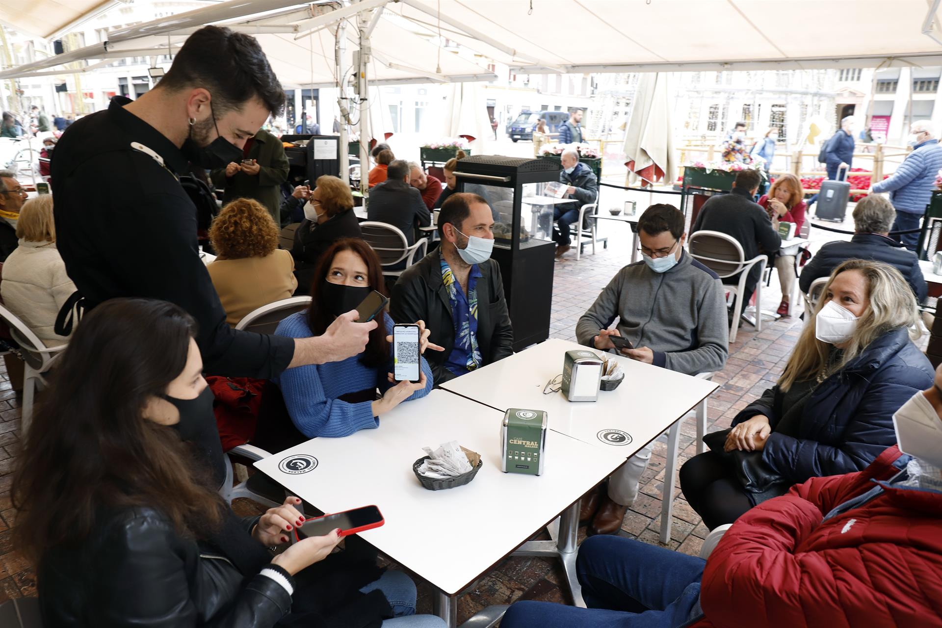 Un camarero pide certificado a los clientes en una mesa de una terraza