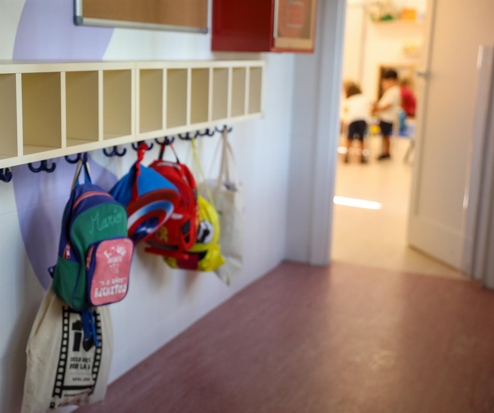 Varias mochilas en una percha de un aula. EP