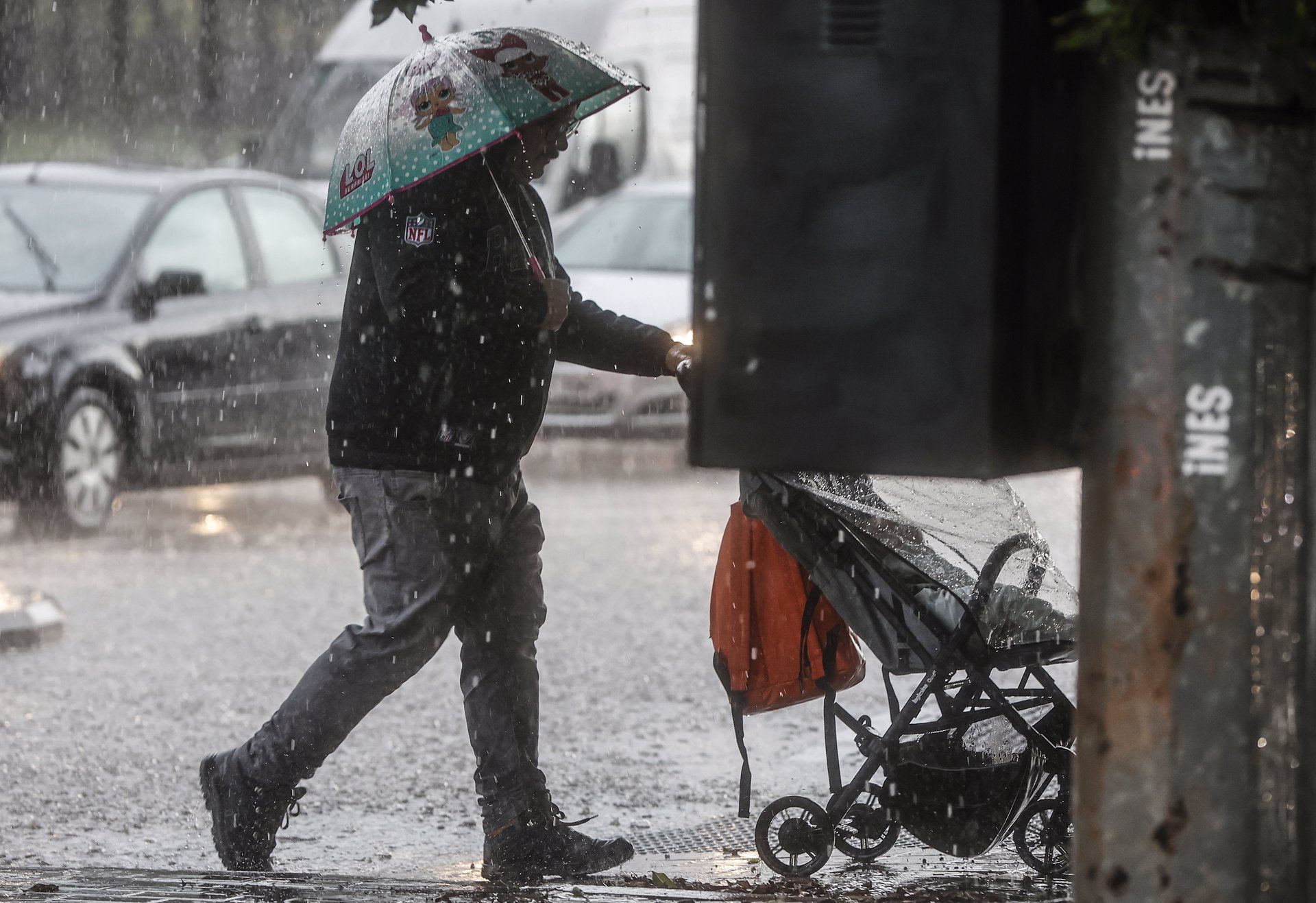 Un hombre lleva un carrito de bebé mientras se protege de la lluvia EP