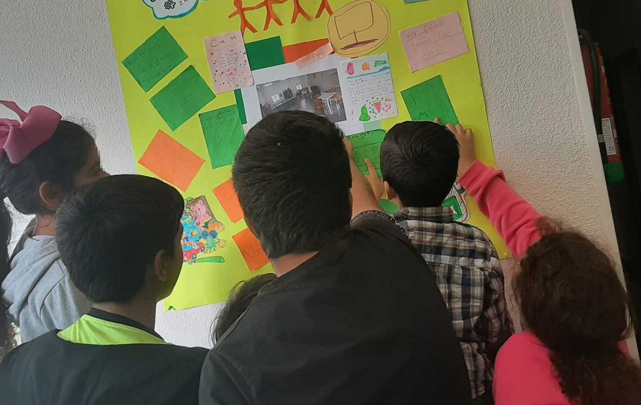 Niños señalan una cartulina en un aula. 